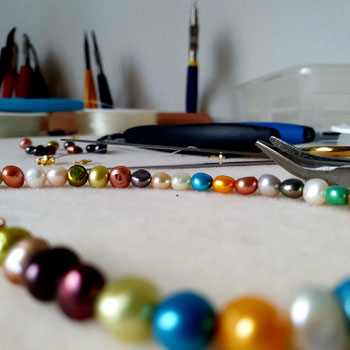 Mala Kette in Reparatur: bunte Perlen und schmuckwerkzeug auf einem Arbeitstisch in liebevoller Vorbereitung für das neue Knüpfen