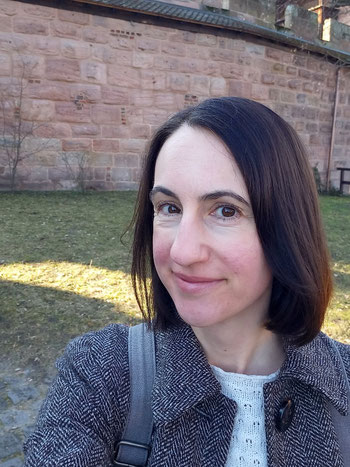Michaela Dauscher steht am Weg vor Burgmauer und lächelt in die Kamera
