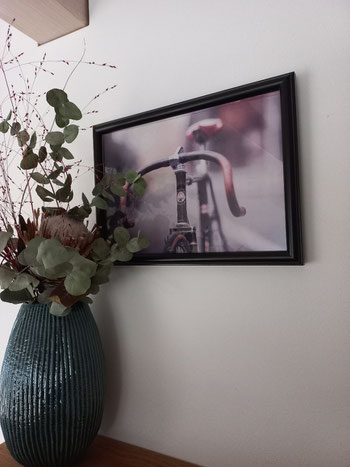 Gesteck steht in Blumenvase vor einem Bild, auf dem ein Rennrad zu sehen ist