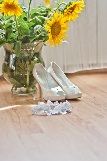 <img src=“Bilddatei.jpg“ alt=Brautschuhe und Kopfschmuck für Braut mit Sonnenblumen in Vase>