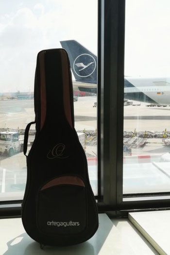Ortega Bass-Ukulele im Gigbag am Flughafen vor einem Flugzeug