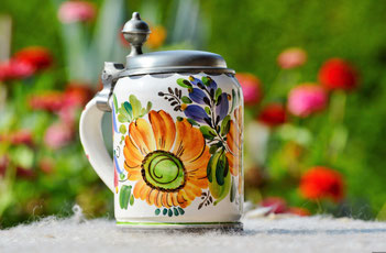 keramischer bunte bemalter Bierkrug mit einer Blumenwiese im Hintergrund