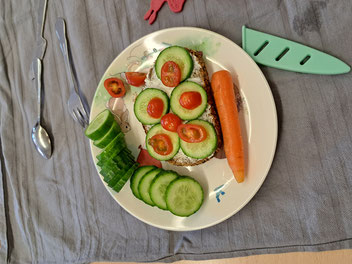 Ein Teller mit einem belegten Brot und verschiedenem Gemüse.