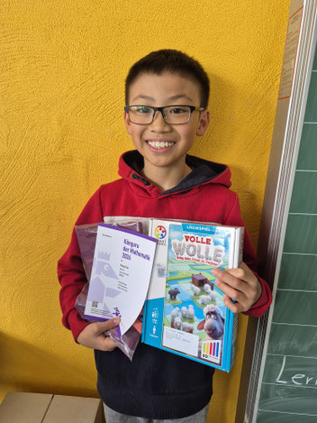 Der Schüler Phong steht vor einer gelben Wan und hält seine Urkunde sowie seinen Preis hoch.