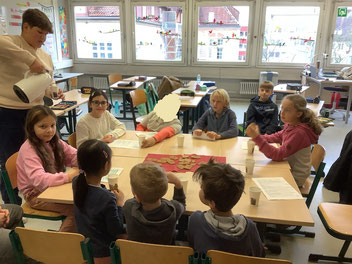Mehrere Grundschüler sitzen mit ein paar Kindergartenkindern an einem Gruppentisch.