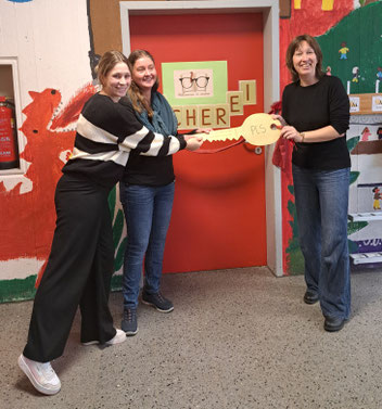 Die Schulleiterin übergibt einen großen Schlüssel an zwei Lehrerinnen vor der neuen Schülerbücherei.