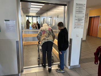 Ein Schüler steigt mit einer älteren Dame in einen Aufzug