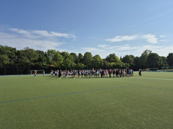 Auf dem Sportplatz stehen viele Kinder in einem großen Kreis.