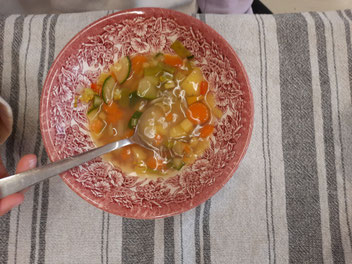 Ein Schale mit Gemüsesuppe und Löffel von oben.