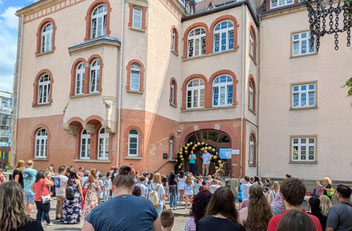 Vor dem Haupteingang der Paul-Lechler-Schule stehen viele Menschen während die Schulleitung eine Rede hält.