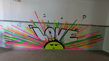 Ein Wandbild mit neonfarbenen Strahlen und einem Smiley über dem Love steht.
