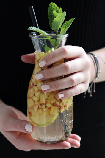 eine Person hält ein Glas Nektarinenbowle
