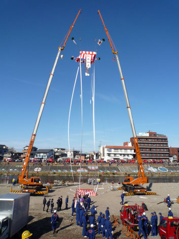 1月に行われる出初式の風景。やぐらに見立てた昭和クレーンの共吊り。（当社のクレーンで吊るした薪から煙があがり、そこにめがけて多くの消防車が一斉に放水をします）