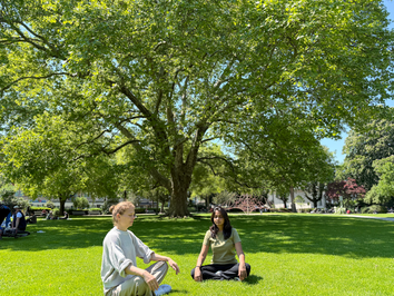 Zwei junge Frauen meditieren im Park der Bäckeranlage in Zürich vor einem grossen Baum
