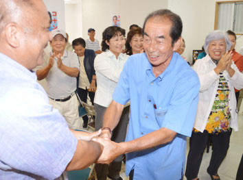 砂川県議と固い握手を交わす西大舛氏。支持者は万歳三唱して当選を祝った=29日、同選対事務所