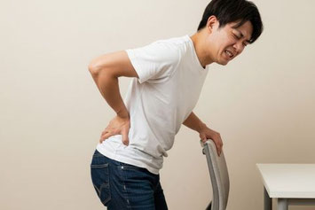 ぎっくり腰で腰に手をあてて痛そうな表情をしている男性の様子