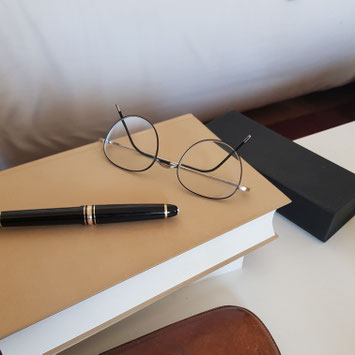 Buch mit Leineneinband, Brille und Füllfeder auf weißem Tisch als Symbol für wissenschaftliche und psychologische Arbeit