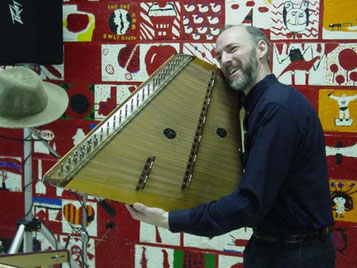 Sam holding up his hammered dulcimer at a school performance, so the audience can see it.