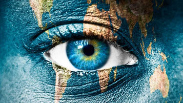 Nahaufnahme eines blauen Auges mit einer Weltkarte, die auf die Haut projiziert oder gemalt ist. Die Darstellung symbolisiert globale Verbundenheit, Empathie und die Fähigkeit, Menschlichkeit zu erkennen und zu erlernen.