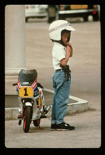 Harry con la sua moto giocattolo sorvegliata da una tata e una guardia del corpo