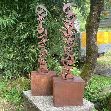 Rustic vertical sculpture by Paolo Grassi composed of stacked oxidized numbers.