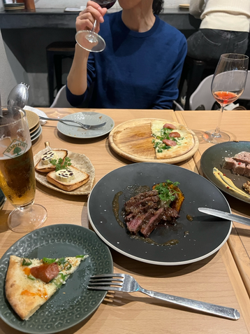 山口県山口市湯田温泉にある炭火イタリアンgrigioにておすすめ料理のお肉やオクラの塩ピザ、レーズンバターを注文し青いセーターを着た女性がワインを飲んでいます。