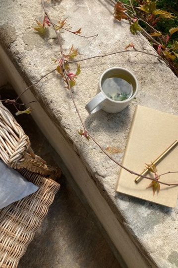 Handgemaakte keramieken mok met een notitieboekje en een pen ernaast in de herfstzon, buiten, slowliving sfeer