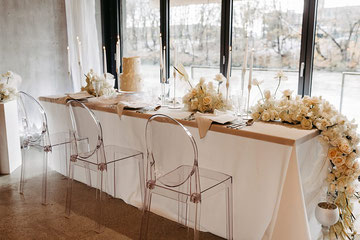 Der Brautpaartisch ist mit Servietten, Blumen, Papeterie, Geschirr und einer weißen Tischdecke geschmückt.