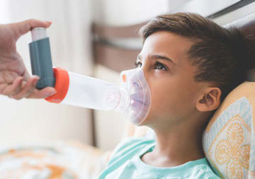 Foto de niño en la cama aspirando un inhalador para el asma