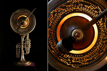 Assemblage light art sculpture made from a silver trumpet, a musical disc from a mechanical player, an oil can, top of a salt shaker, illuminated within a copper concave dish.