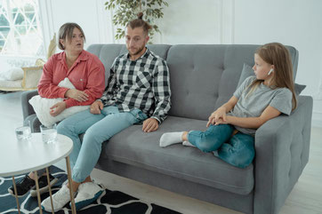 Vater, Mutter und Tochter sitzen aiuf dem Beratungssofe, Stimmung ist angespannt, Tochter sitzt mit Abstand und trägt Kopfhörer