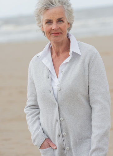Naturfarbende längere Strickjacke aus Schurwolle in der Farbe natur getragen über einer schlichten weissen Bluse.