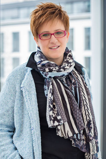 Julia Lakirdakis-Stefanou, Inhaberin von juliaandfriends.de, mit roter Brille, kurzem Haar und gemustertem Schal – offen, kompetent und nahbar.