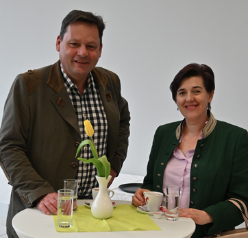 Mann und Frau im traditionellen Outfit bei einem Stehtisch mit Getränken – Frühlingshafte Tischdeko mit gelber Tulpe.