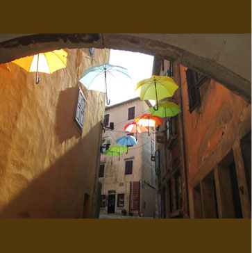 Dieses Bild zeigt bunte Regenschirem in einer Altstadt. Diese können an den Film "Mary Poppins" erinnern.