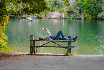 Eine Person liegt an einem Fluss und liest.