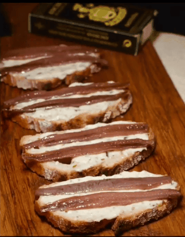 Foto de un plato con cuatro triángulos de pan tostado, cada uno con un filete de anchoa Bolado y una cucharada de salsa tártara, espolvoreados con cebollino picado.