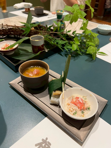 石川県にある福喜寿司にてコース料理を注文し、前菜にカニサラダと冷やし茶碗蒸し、笹の葉に巻かれたお寿司がテーブルに並んでいます