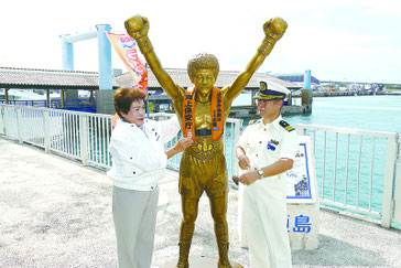 具志堅用高像にライフジャケットをつける石垣海上保安部の中村次長と海上保安協会の辻野ヒロ子支部長=15日午前、離島ターミナル