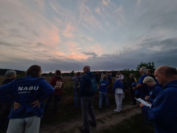 Eine Gruppe von Menschen in NABU-Kleidung steht im Sonnenuntergang