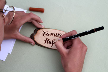 Familienname wird per Handlettering auf eine ovale Holzscheibe aus Eschenholz geschrieben.