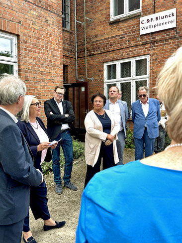 Ministerin Stenke spricht vor den Gebäuden der  Wollspinnerei, zusehen außerdem Ole Plambeck MdL, Monika Saggau, Toni Köppen und Jörg Buthmann.