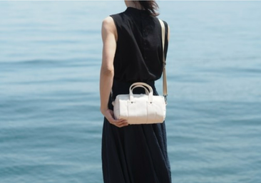 高松市サンポートの海の前で、黒い服を着た女性が生成りの帆布ミニボストンバッグのshort ducksを斜め掛けしている