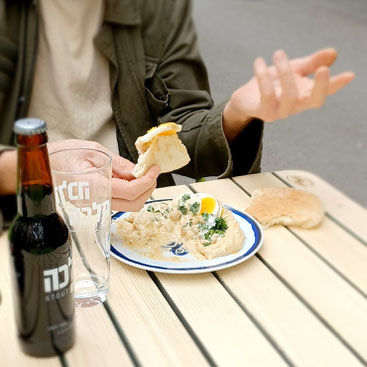 Ein Gast isst unseren hausgemachten Hummus und trinkt ein Bier von Malka dazu. Der Gast sitzt in unserer Gartenwirtschaft.