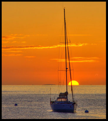 Au soleil levant, en pleine mer un voilier se détache de l'horizon 