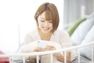 自宅のソファからスマートフォンを見る女性