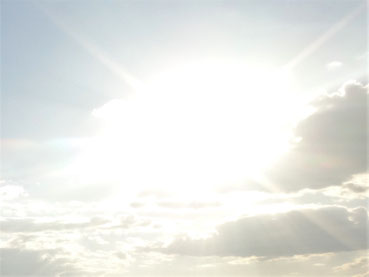 Weiße Wolke am Himmel, die durch die dahinter stehende Sonne sehr hell strahlt und vier Strahlen in vier Richtungen abgibt