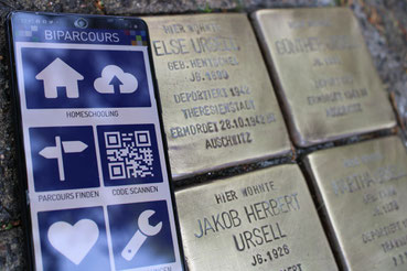 Handy mit Biparcours-App neben vier Stolpersteinen