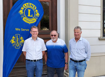Drei Männer neben eine Lions Club-Fahne.