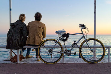;image d'un couple assis sur un banc a coté d'un vélo entrain de regarder la mer.